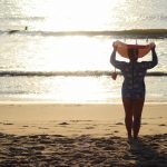 Person carrying a surfboard on a beach at sunset.