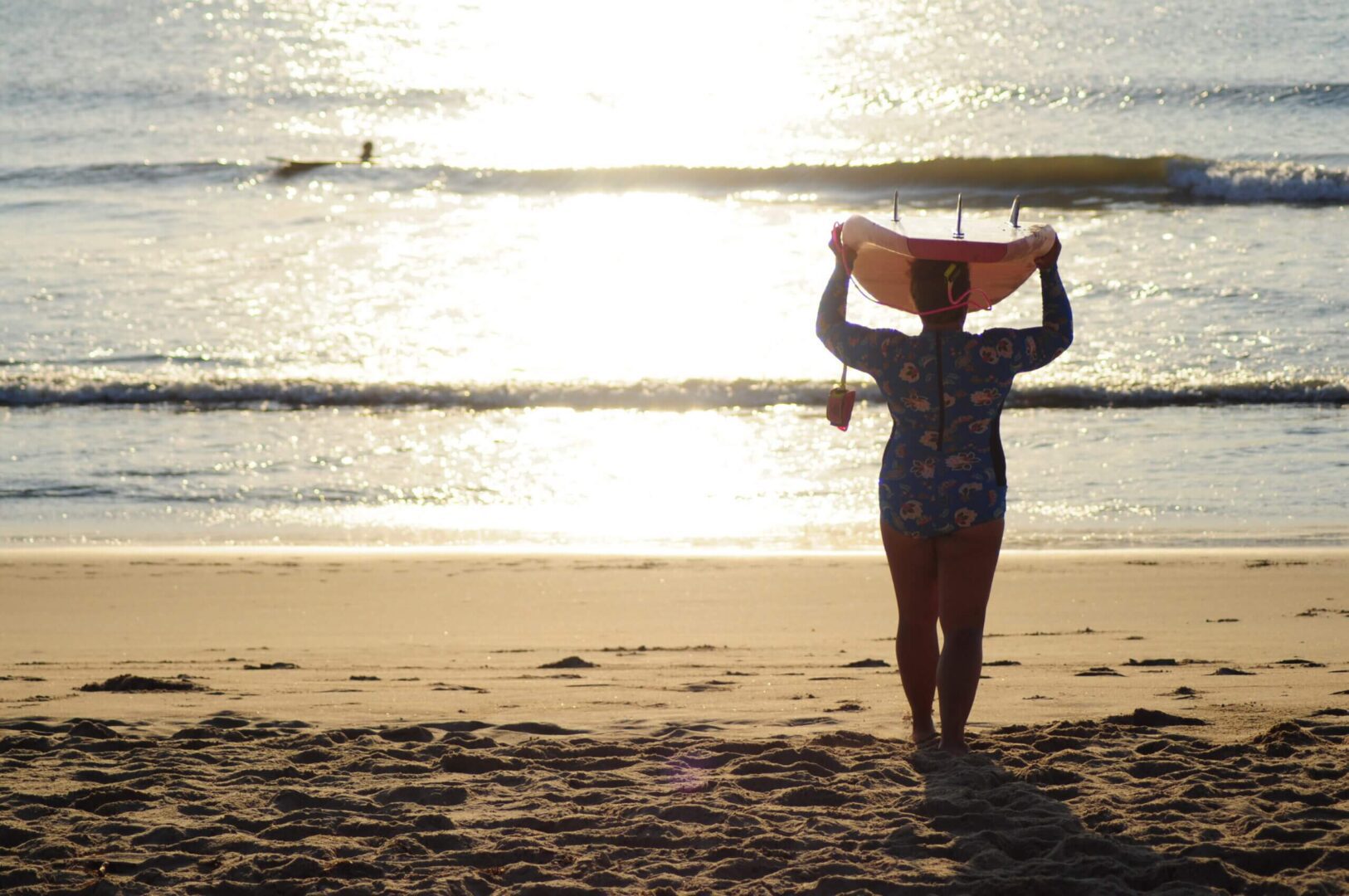 Person carrying a surfboard on a beach at sunset.