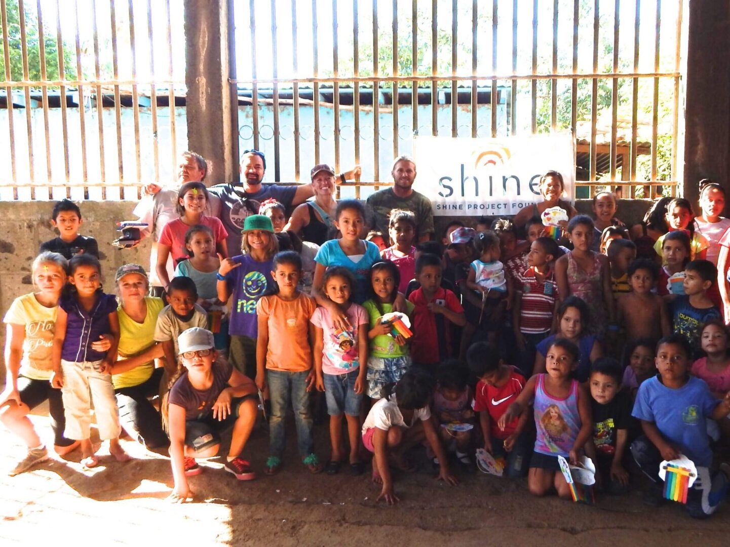 Group of smiling children and adults posing outdoors by a lake with a banner.