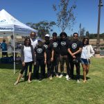Group of six people posing outdoors at a sunny event.