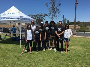 Group of six people posing outdoors at a sunny event.