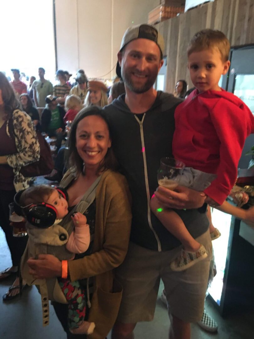 A happy family posing indoors with their two children, one in a stroller and the other held in arms.