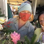 Two people smiling, one wearing a mask and holding flowers.