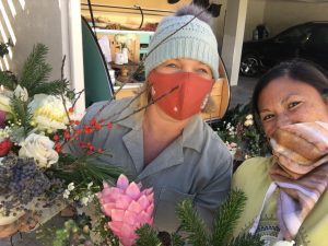 Two people smiling, one wearing a mask and holding flowers.