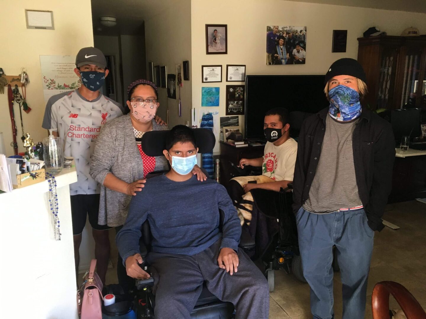 Four men wearing masks in a room, one seated in a wheelchair.