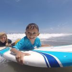Smiling children enjoying surfing on a sunny beach day.