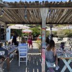 Outdoor rustic restaurant with people dining under a wooden pergola.