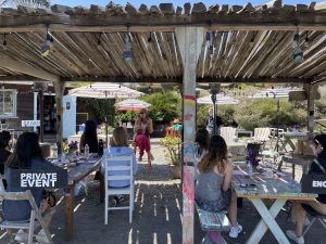 Outdoor rustic restaurant with people dining under a wooden pergola.