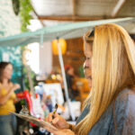 Blonde woman writing in a notebook at a cafe.