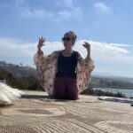 Person practicing yoga outdoors with scenic background and clear sky.