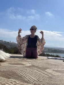 Person practicing yoga outdoors with scenic background and clear sky.
