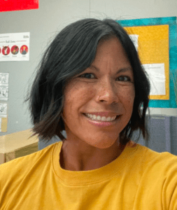 Smiling woman with short dark hair wearing a yellow shirt.