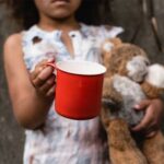 Child holding a red cup and a teddy bear.