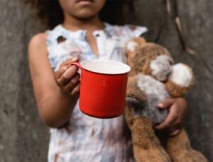 Child holding a red cup and a teddy bear.
