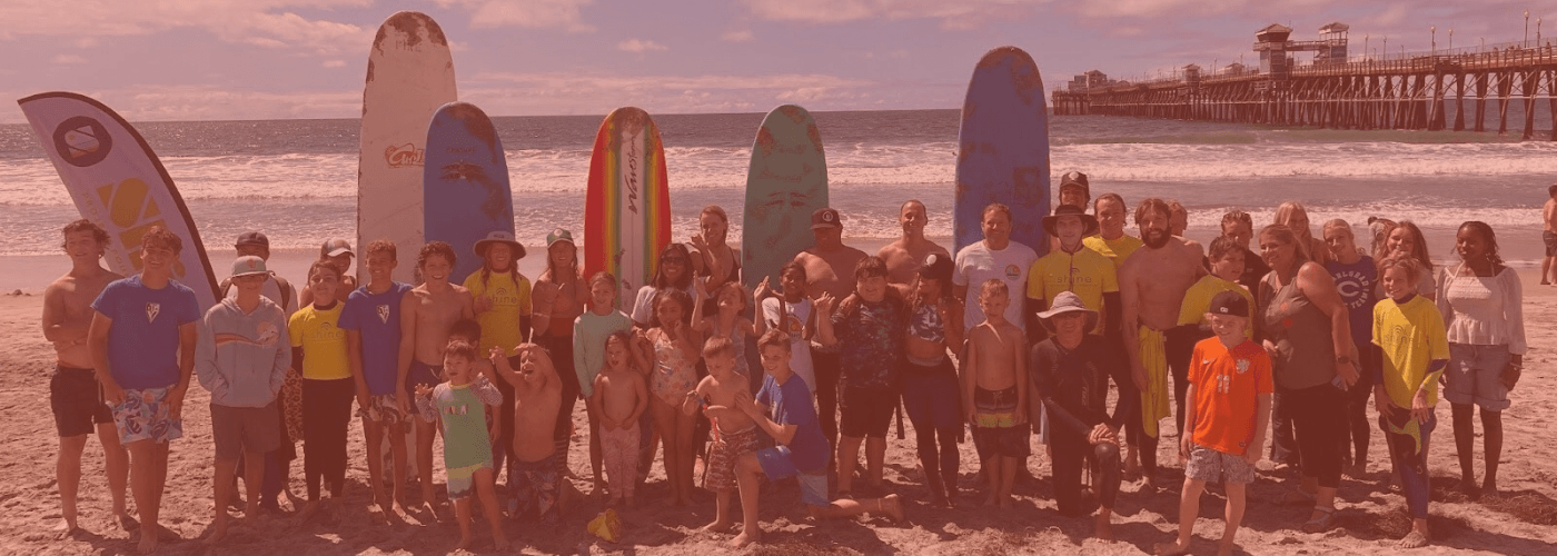 Group of people posing with surfboards on a beach at sunset.