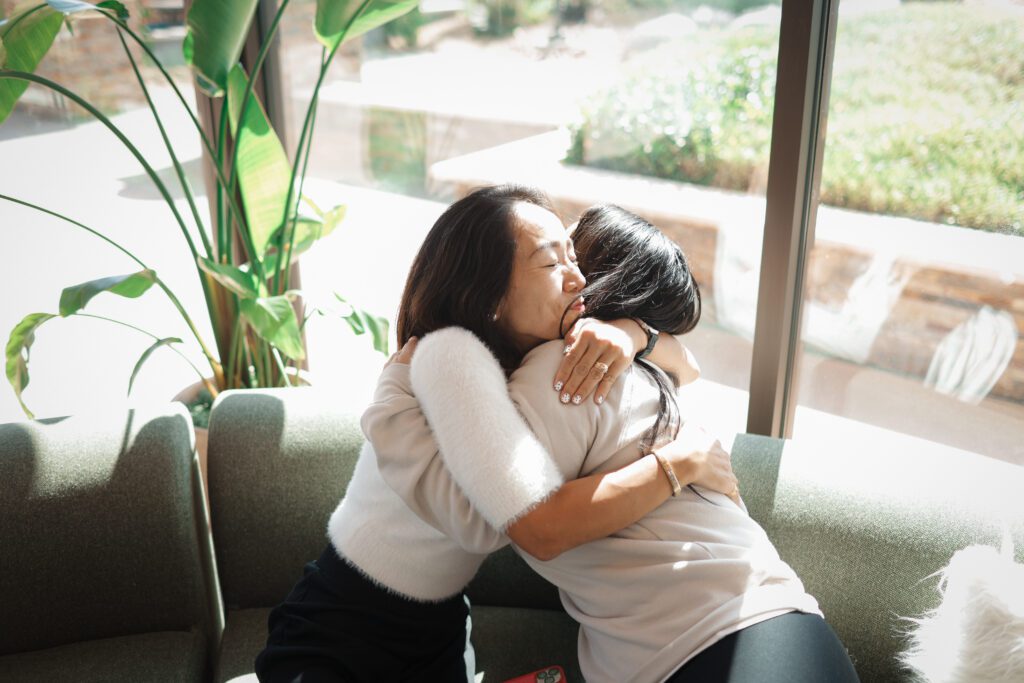 Women embrace warmly on sunlit sofa