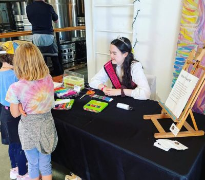 A woman at a craft booth interacts with two children.