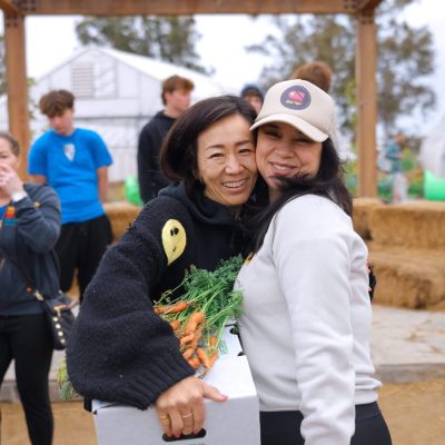 Two women hugging with box of carrots