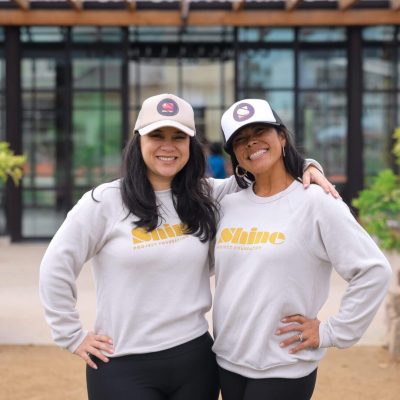 Two women smiling and posing in matching white sweatshirts and hats.
