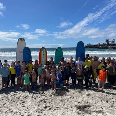 Group of people with surfboards posing on the beach near the ocean.