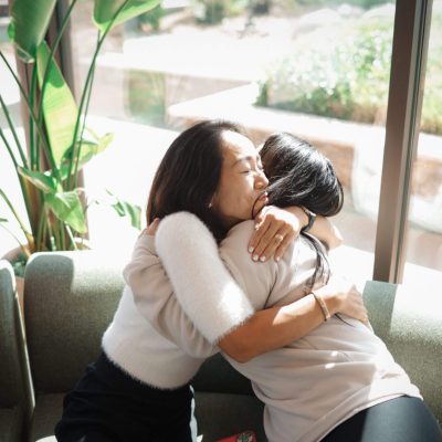 Women embrace warmly on sunlit sofa