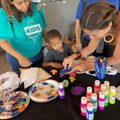Children and adults painting colorful designs on black paper.