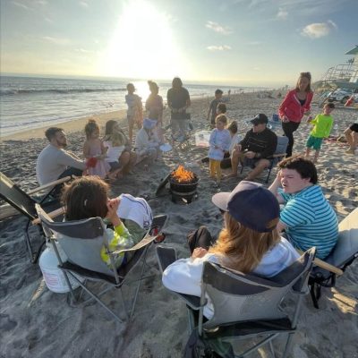 Group of people around a bonfire on the beach at sunset.