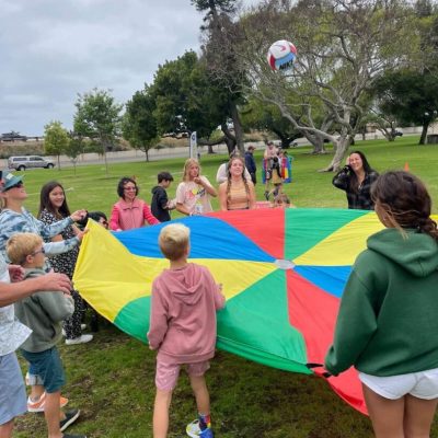 Children playing with a colorful parachute outdoors.