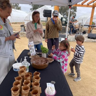 Family enjoying a food tasting event outdoors under a tent.