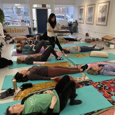 Group yoga class with participants lying on mats in a studio.